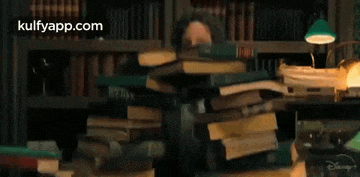 a man is sitting at a desk with a stack of books .