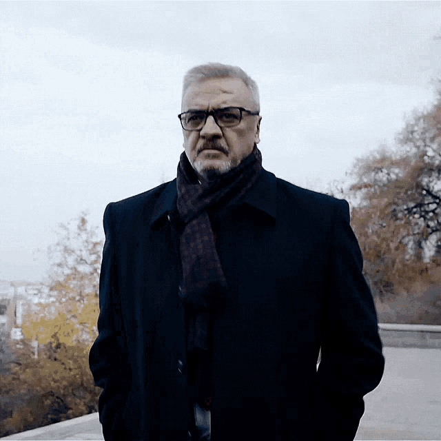 a man wearing glasses and a scarf is standing in the dark