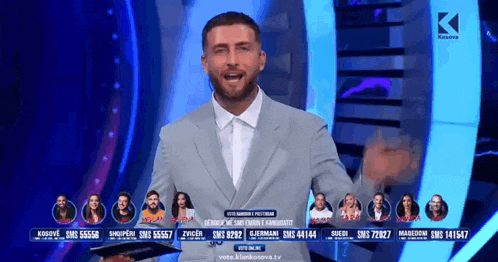 a man in a suit is standing in front of a screen that says vote.klankosova.tv