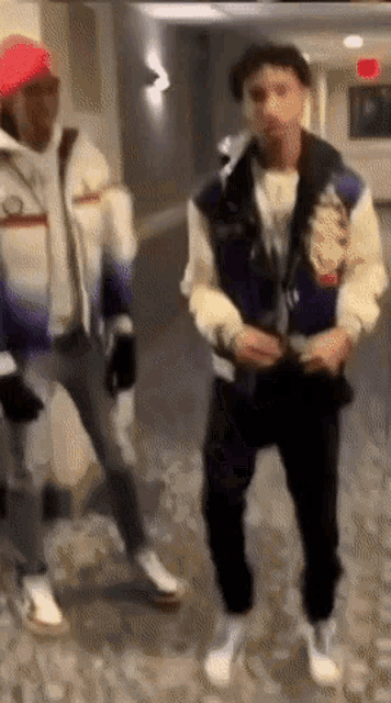 two men are dancing in a hallway and one is wearing a purple jacket