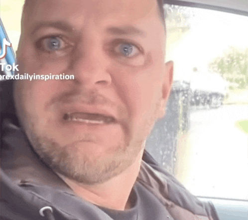 a man with a beard is sitting in a car and making a funny face