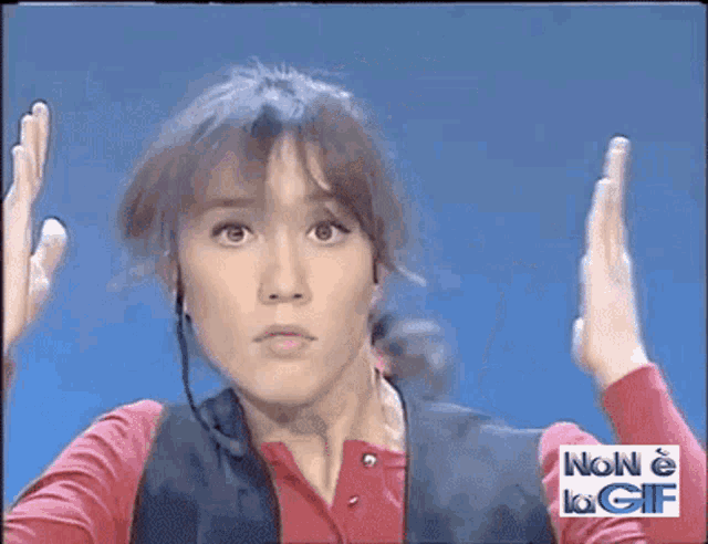 a woman wearing headphones holds her hands up in front of a sign that says non è la gif