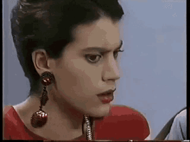 a woman wearing red earrings and a red shirt is looking at the camera .