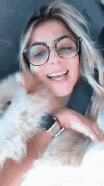 a woman wearing glasses is holding a small white dog and smiling