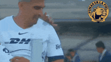 a man in a pumas en la piel jersey is holding a trophy