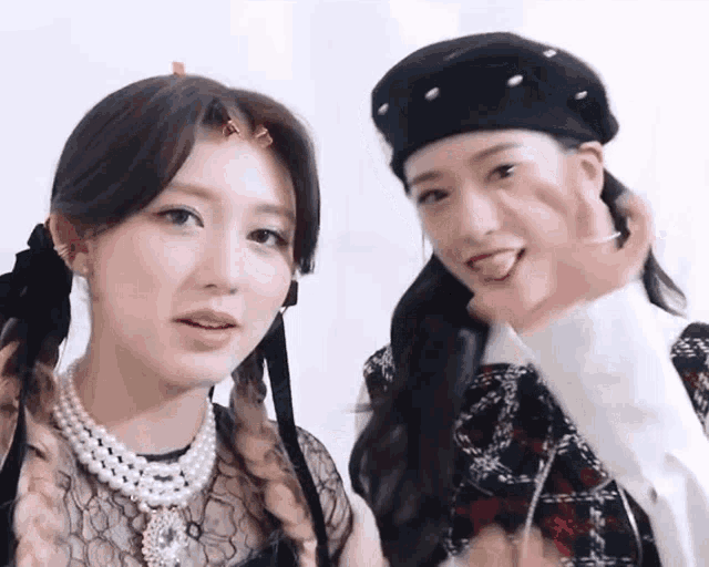 two women are standing next to each other and looking at the camera . one of the women is wearing a pearl necklace .