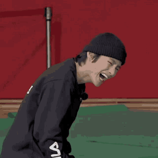 a man wearing a black fila sweatshirt is laughing while wearing a black beanie .