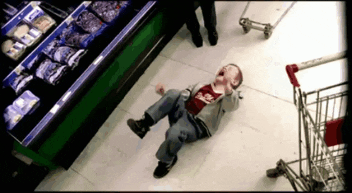 a young boy is laying on the floor in a grocery store wearing a shirt that says ' eagles '