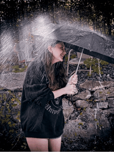 a woman holding an umbrella in the rain while wearing a sweatshirt that says ' infinity '