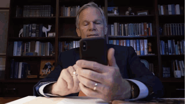a man in a suit is looking at a cell phone in front of a bookshelf with a picture of a camel on it