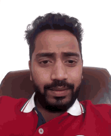 a man with a beard is sitting in a chair wearing a red polo shirt .