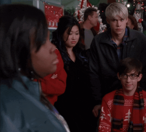 a group of people are gathered in a room with a christmas tree in the background