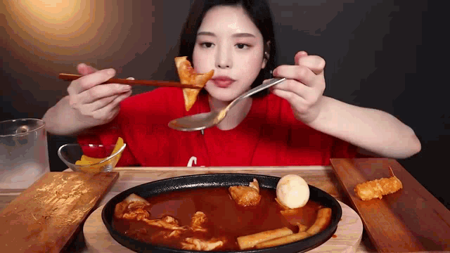 a woman in a red shirt is eating a plate of food with chopsticks and a spoon