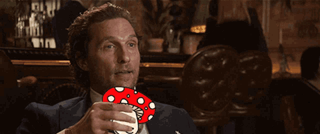 a man in a suit and tie is drinking from a red cup with white polka dots
