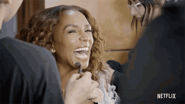 a woman is laughing while getting her makeup done with a netflix logo in the background