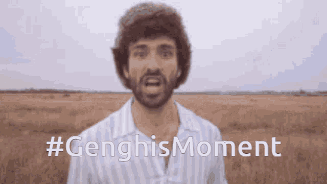 a man with a beard is standing in a field with the hashtag #genghismoment written below him