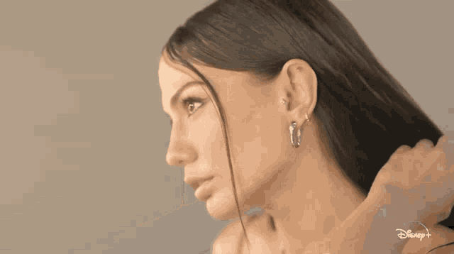 a woman wearing hoop earrings is looking at her hair in front of a disney logo
