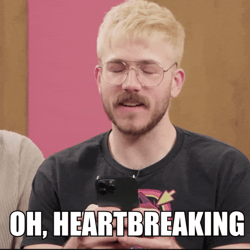 a man with glasses and a mustache holds a cell phone and says " oh heartbreaking "