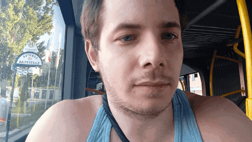 a man wearing a blue tank top is looking at the camera with a sign in the background that says autobus haltesstelle