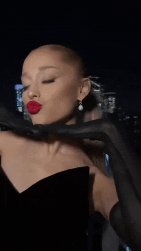 ariana grande is wearing a black dress and red lipstick while holding a black glove .