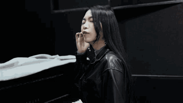 a woman wearing a black leather jacket and earrings stands in front of a piano