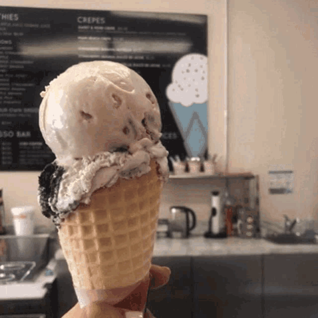 a person is holding a cone of ice cream in front of a menu that says crepes