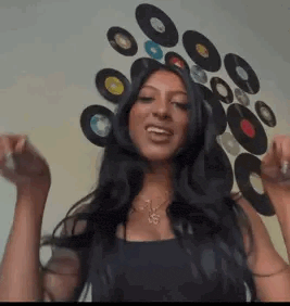 a woman with long black hair is standing in front of a wall of records .