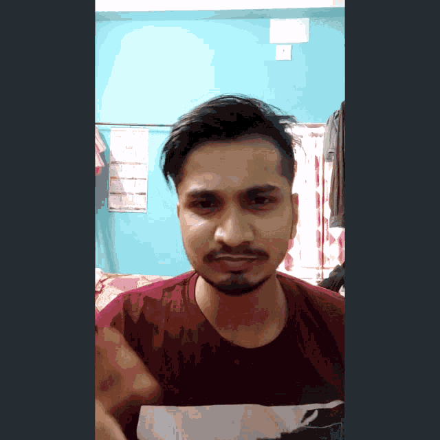 a man with a beard wearing a maroon shirt is making a face