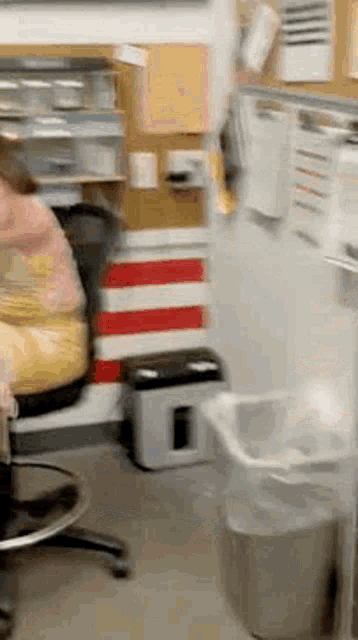 a woman is sitting in a chair in an office with a trash can in the foreground .