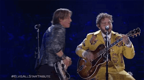 a man in a yellow jacket singing into a microphone next to a man in a silver jacket
