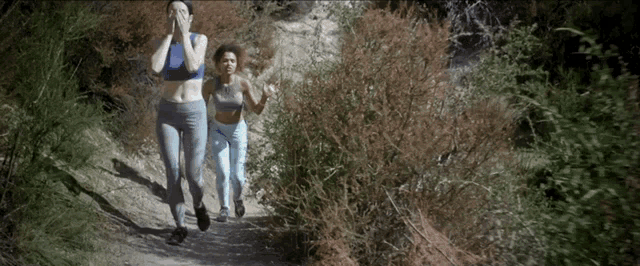 two women are running down a dirt path with trees in the background