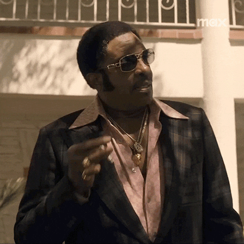 a man wearing sunglasses and a suit is smoking a cigarette .