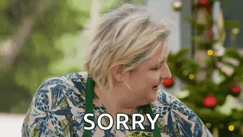 a woman is saying sorry in front of a christmas tree