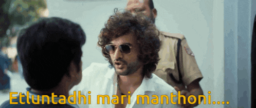a man wearing sunglasses talks to another man with the words " ettuntadhi mari manthoni " behind him