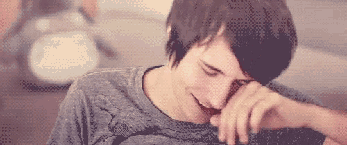 a young man is sitting on a couch laughing while covering his mouth with his hand .
