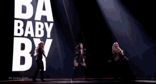 a group of three women singing on a stage in front of a large b
