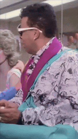 a man wearing sunglasses and a purple shirt sits in a chair