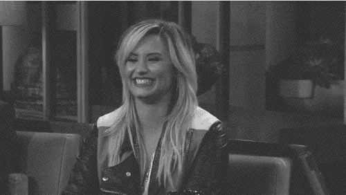 a black and white photo of a woman smiling while wearing a leather jacket .
