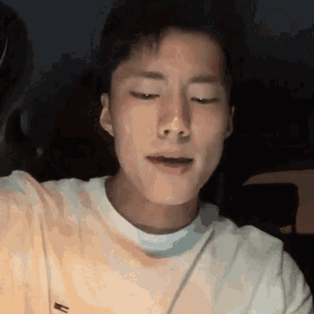a young man wearing a white t-shirt is taking a selfie with his eyes closed .