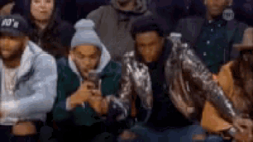 a group of people sitting in a stadium looking at their cell phones .