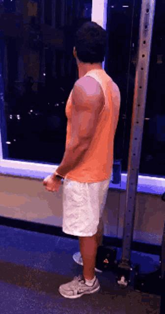 a man in an orange tank top is standing in front of a window