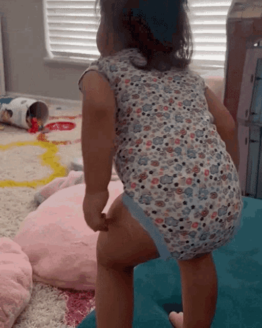 a little girl wearing a floral bodysuit is standing on a blue pillow