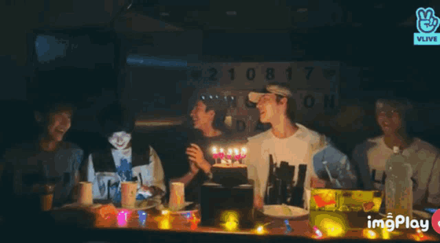 a group of young men are standing around a table with a cake and a sign .