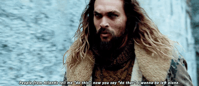 a man with long hair and a beard is standing in front of a body of water .
