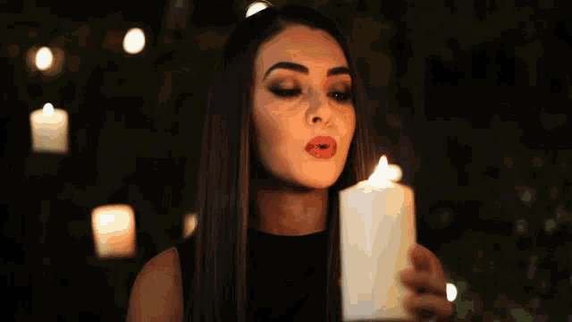 a woman blows out a candle in front of a row of lit candles