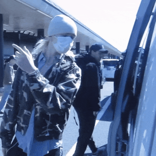 a woman wearing a mask and a white beanie is standing in front of a van