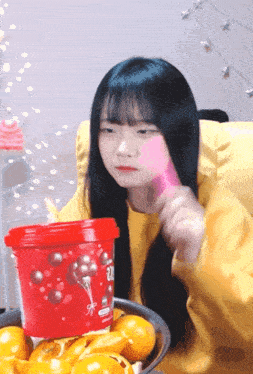 a girl in a yellow sweater is sitting in front of a bowl of oranges and a red container that says 20