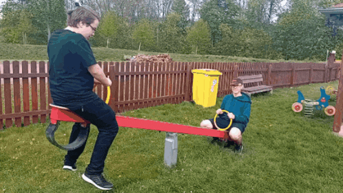 two boys playing on a seesaw with a yellow bin in the background