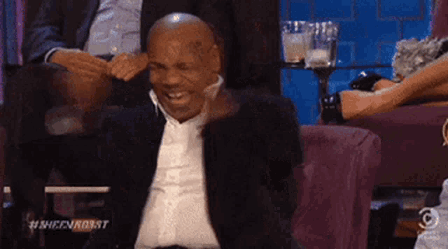 a man in a suit is sitting in a chair with his hands on his head .