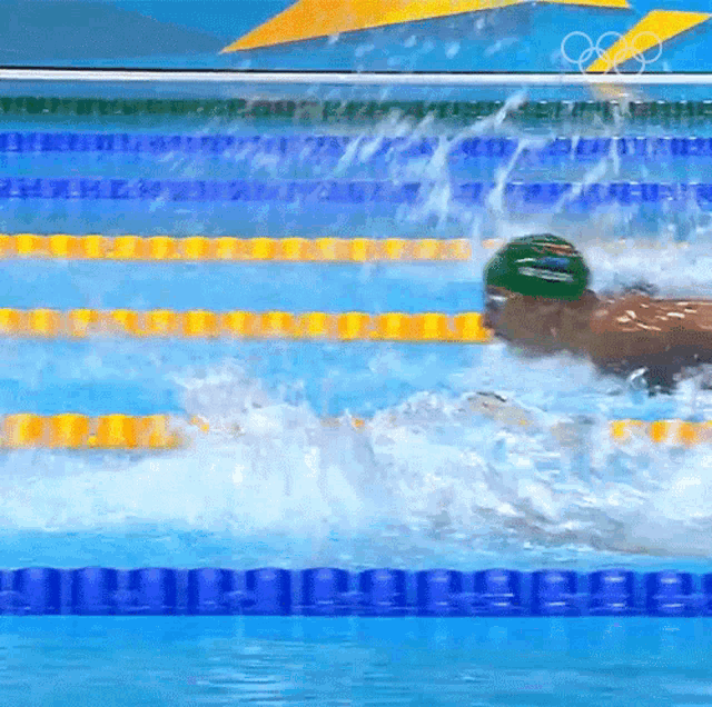 a man is swimming in a pool with the olympic rings on the wall behind him